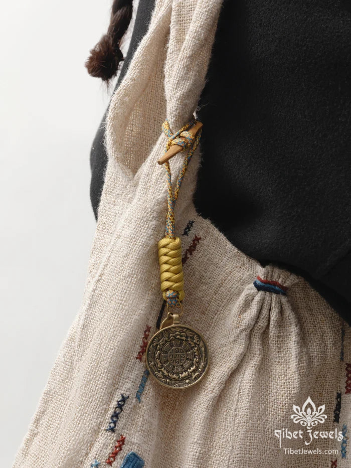 Tibetan bagua brass charm clipped to a leather backpack as a protective amulet.