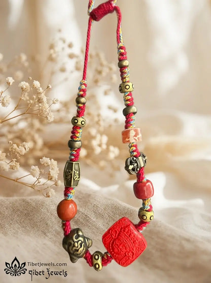 Close-up of carved red cinnabar Zashi Lhamo deity bead and antique brass Garuda and mantra charms