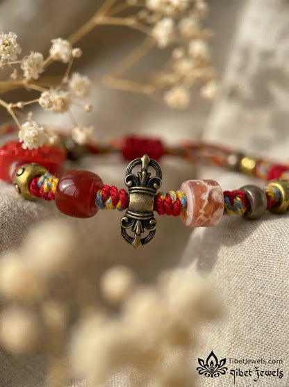 Close-up of carved red cinnabar Zashi Lhamo deity bead and antique brass Garuda and mantra charms