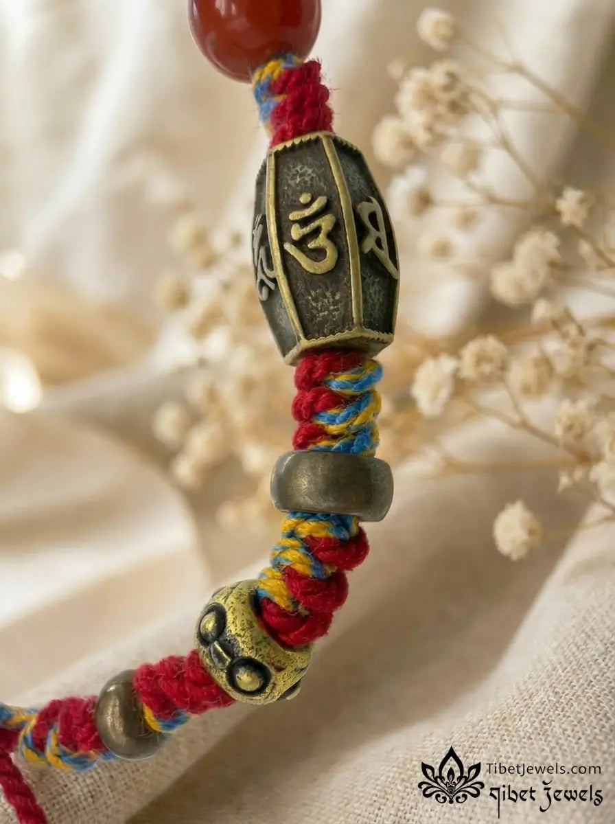 Close-up of carved red cinnabar Zashi Lhamo deity bead and antique brass Garuda and mantra charms