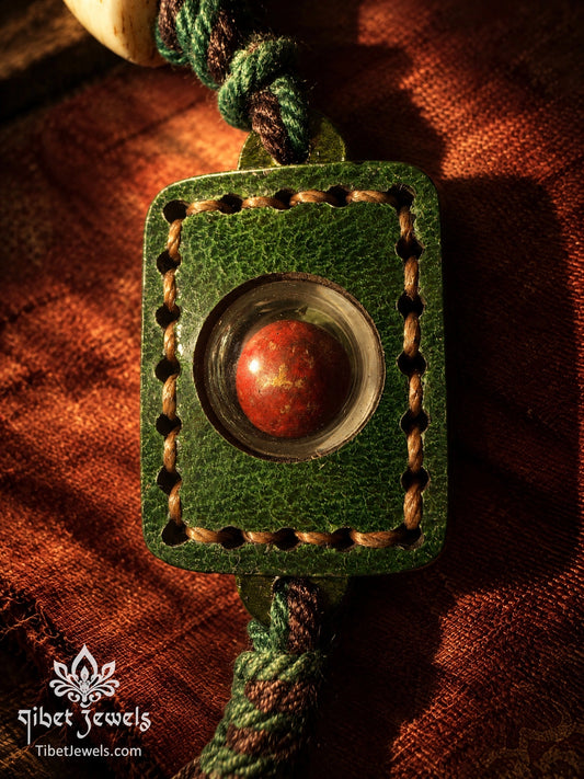 Green leather amulet with hand-stitched border and a domed window sealing cinnabar and Tibetan herbs