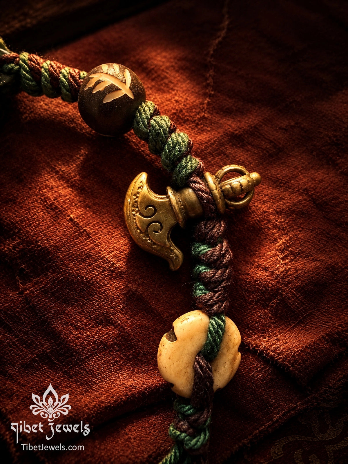 Copper vajra charm and carved yak bone beads on a hand-braided green and plum cord bracelet