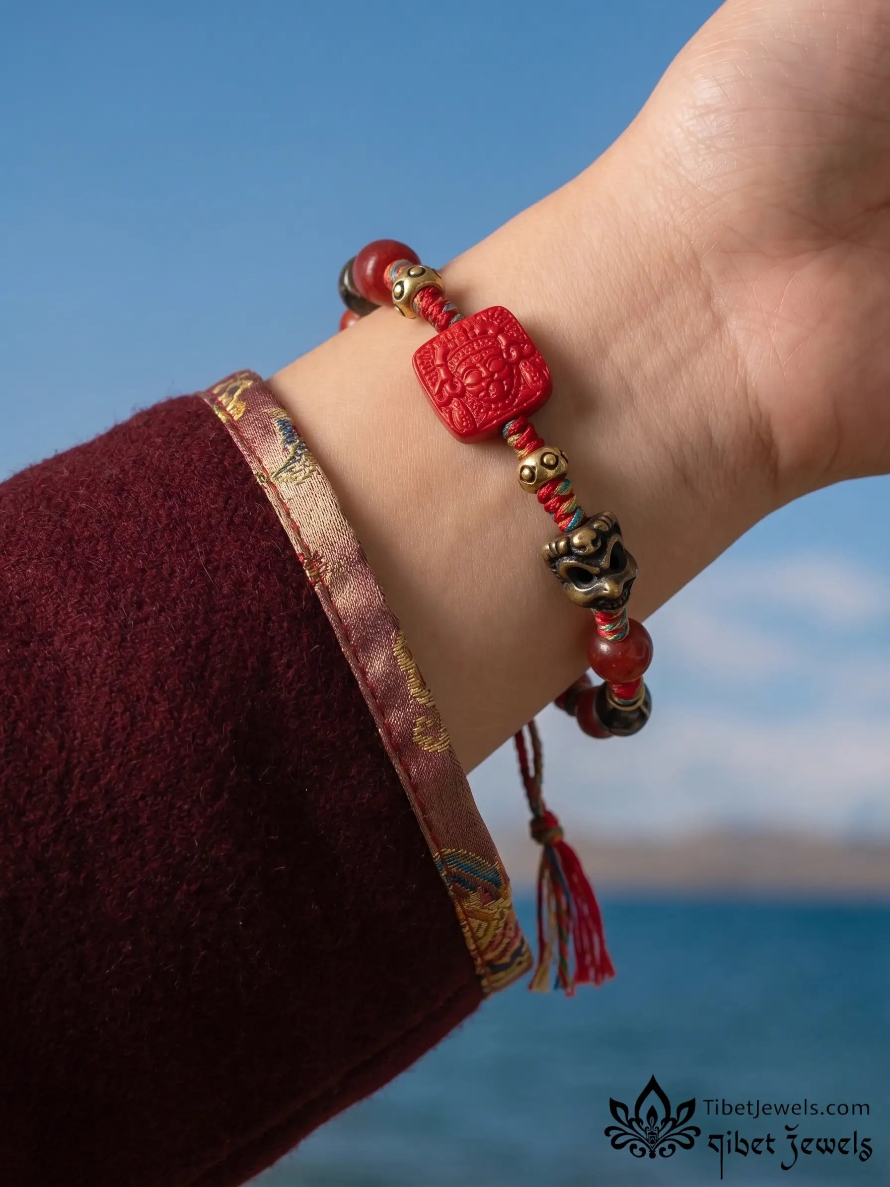 Close-up of carved red cinnabar Zashi Lhamo deity bead and antique brass Garuda and mantra charms