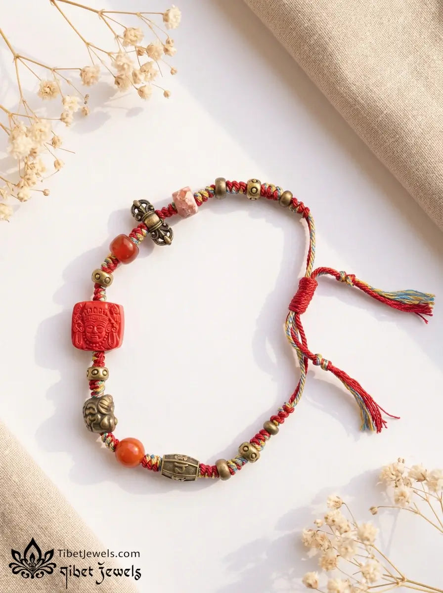 Close-up of carved red cinnabar Zashi Lhamo deity bead and antique brass Garuda and mantra charms