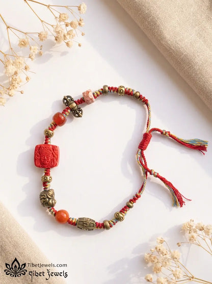 Close-up of carved red cinnabar Zashi Lhamo deity bead and antique brass Garuda and mantra charms