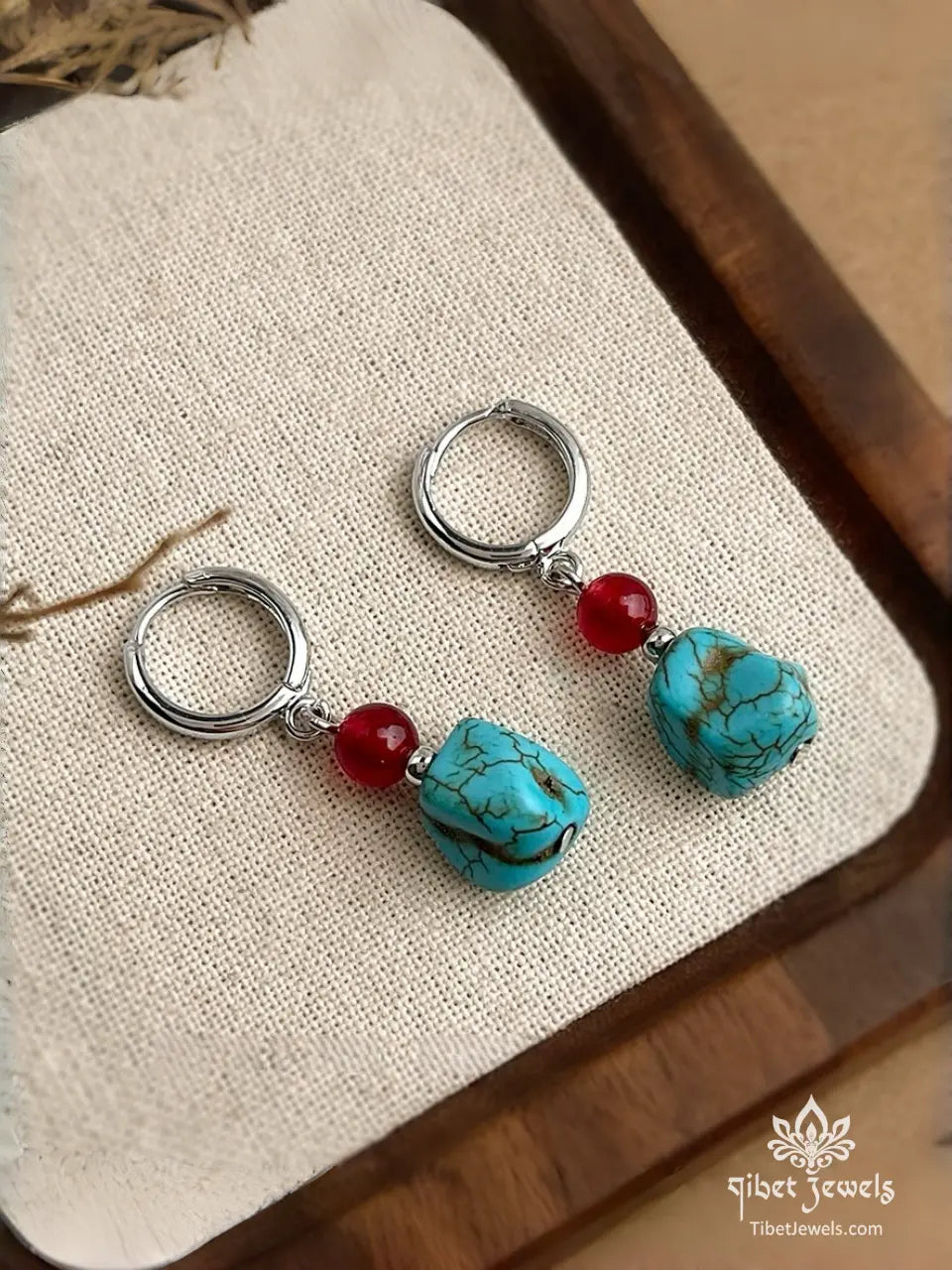 Close-up of natural turquoise stone and red agate bead on a silver-plated huggie hoop.