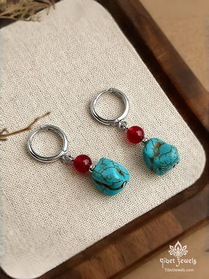 Close-up of natural turquoise stone and red agate bead on a silver-plated huggie hoop.